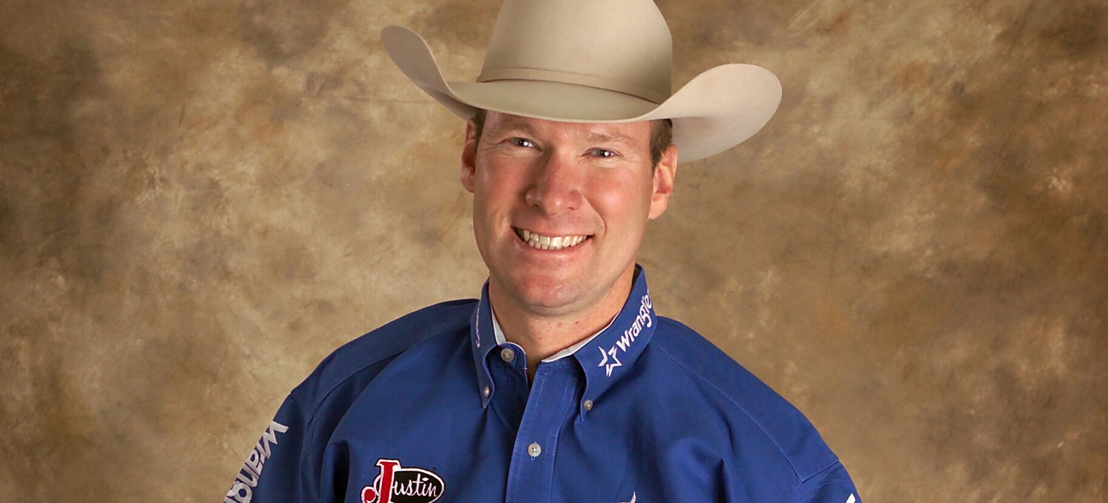 A cowboy, Wayne Brooks, wearing a blue shirt and smiling.